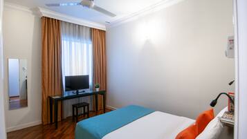 Una habitación de hotel con una cama, un escritorio con computadora, televisión y ventilador de techo.
