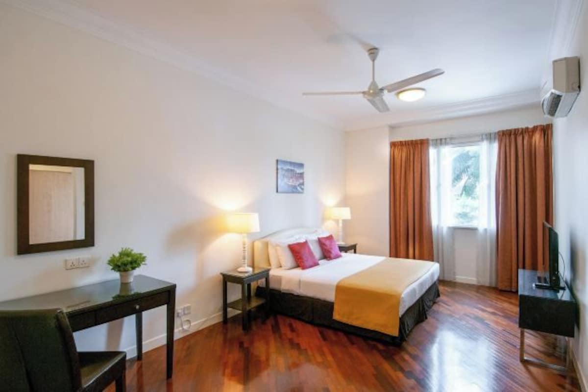Habitación de hotel con cama, mesitas de noche, escritorio, silla, ventilador de techo y ventana con cortinas.