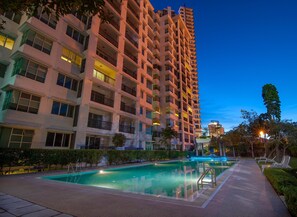 Un hotel moderno de altura con múltiples balcones, una piscina y un jardín bien cuidado.