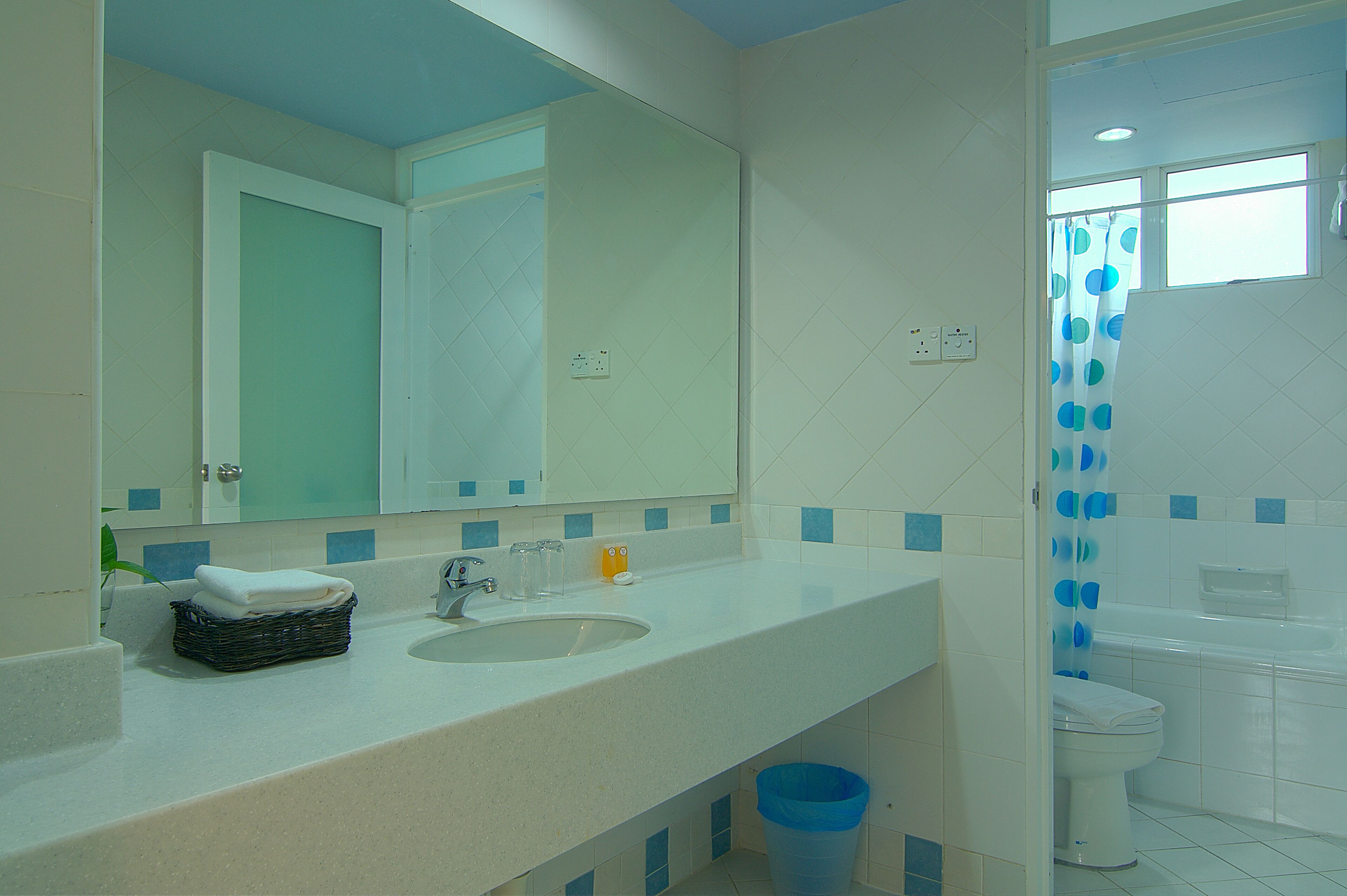 A bathroom with a white sink, mirror, and toilet. There is a blue trash bin under the sink.