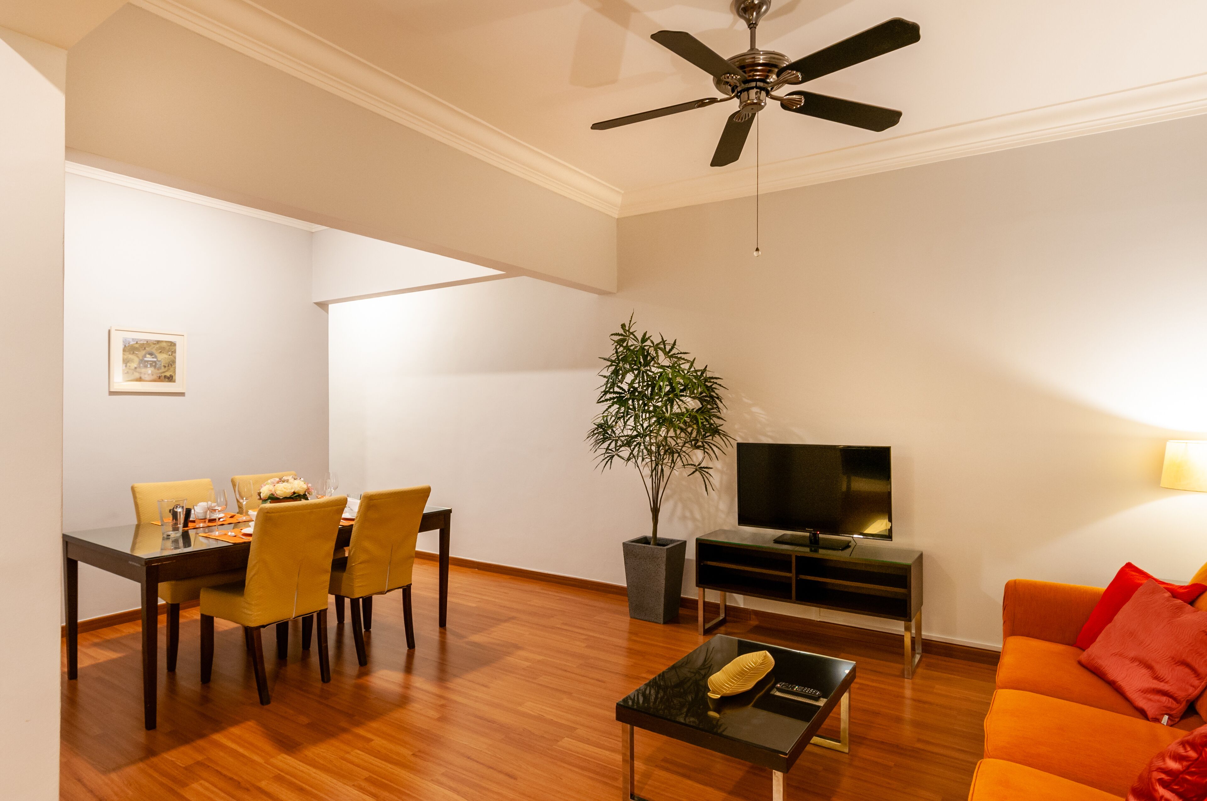 A modern living room with a dining area, a flat-screen TV, a ceiling fan, and a potted plant.