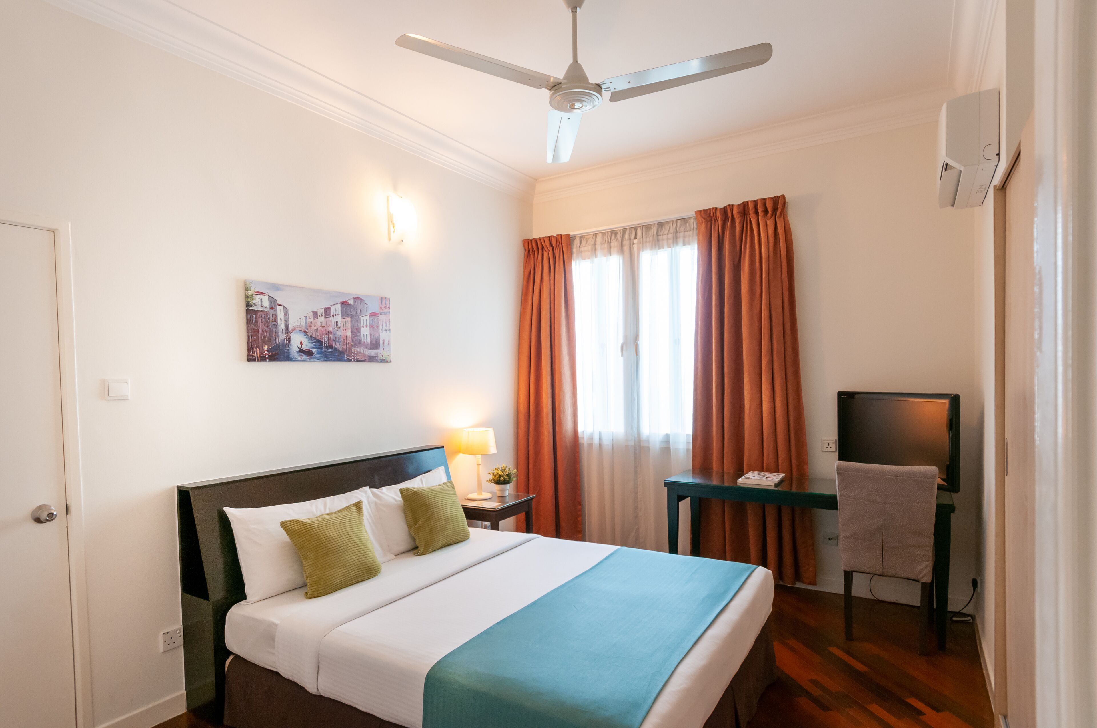 Una habitación de hotel con cama, escritorio y silla, televisión y un cuadro en la pared.