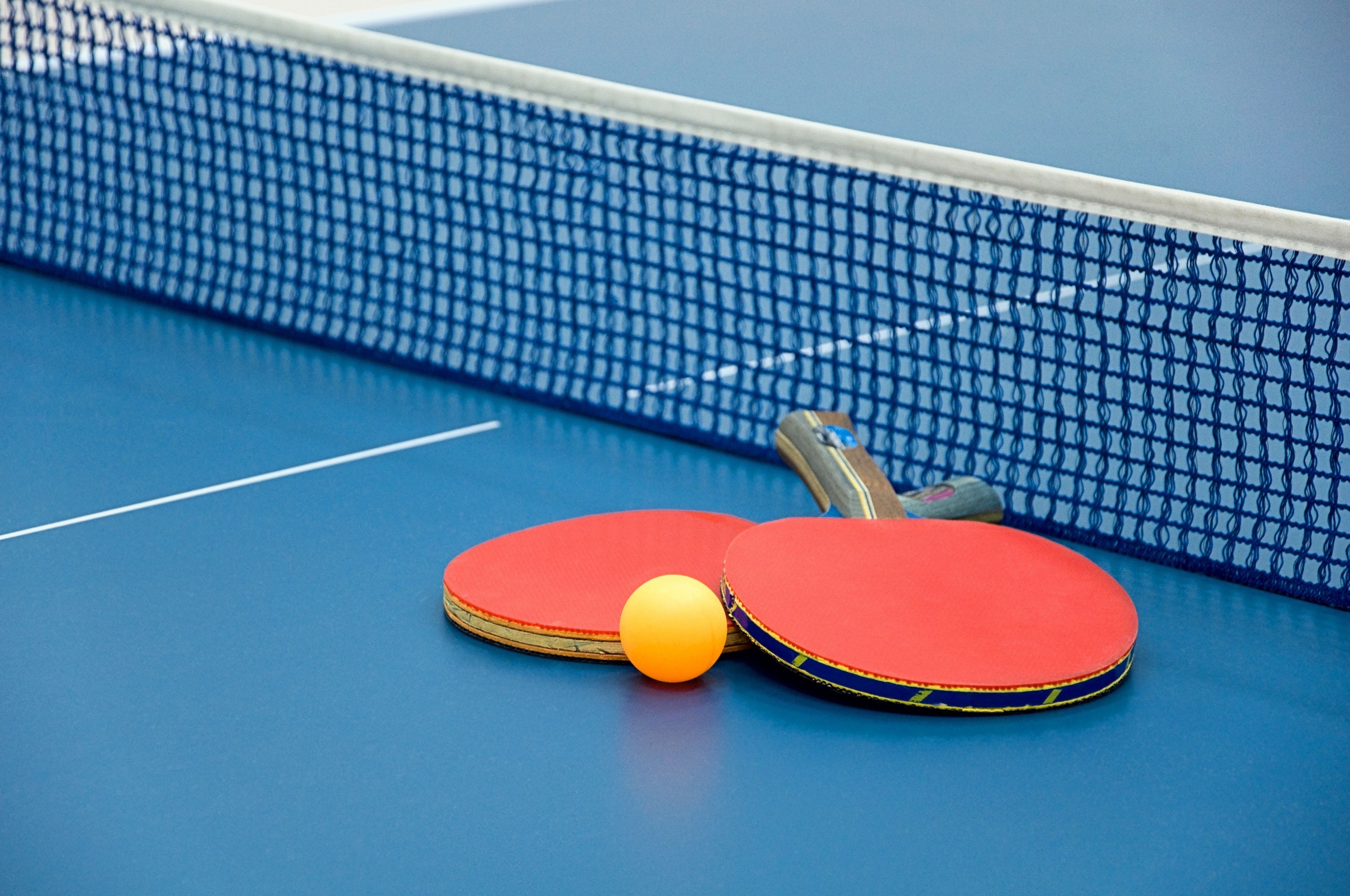 A blue table tennis table with two red paddles and a yellow ball.