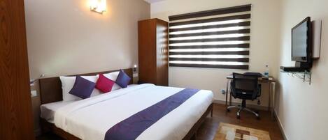 A hotel room with a bed, a desk, a chair, a television, and a window with blinds.