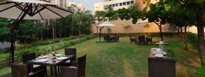 Un'area pranzo all'aperto con tavoli e sedie, circondata da vegetazione e un edificio sullo sfondo.