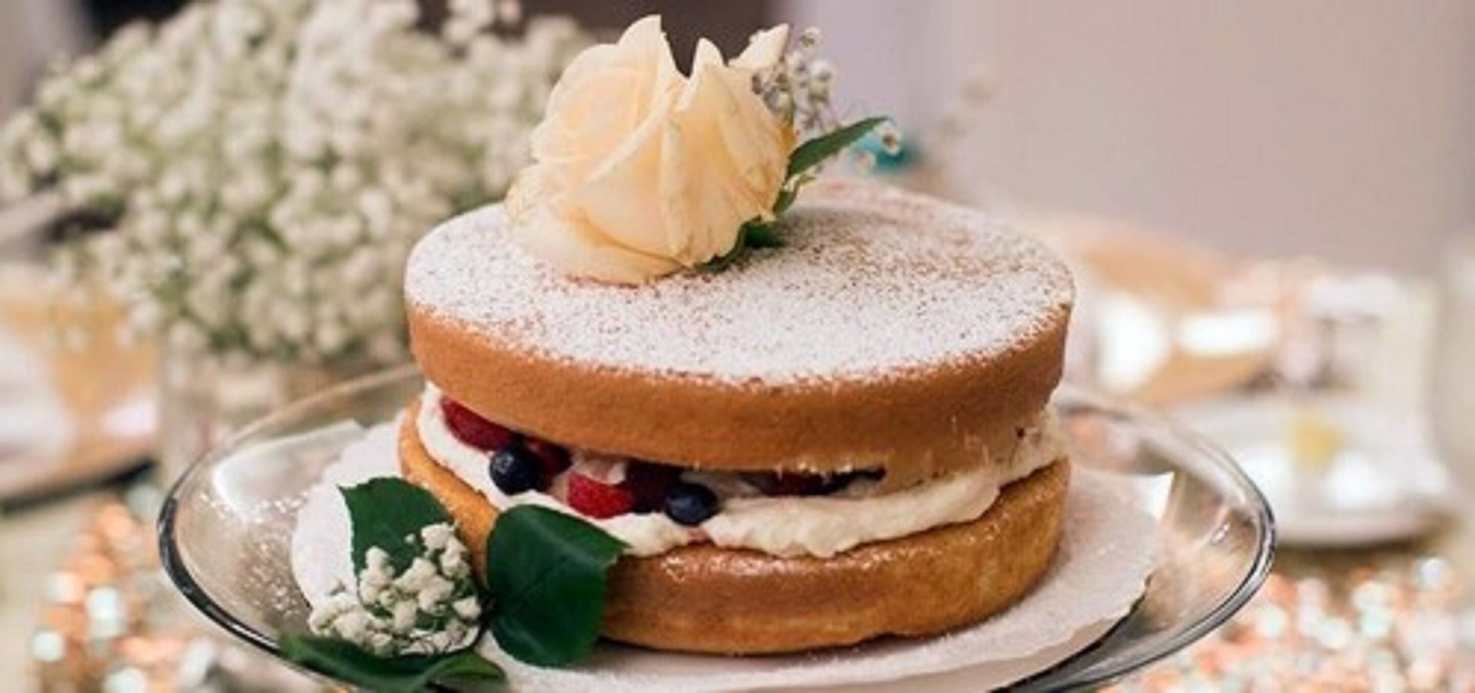 A dessert with a powdered topping and a single flower on top, served on a clear glass plate.