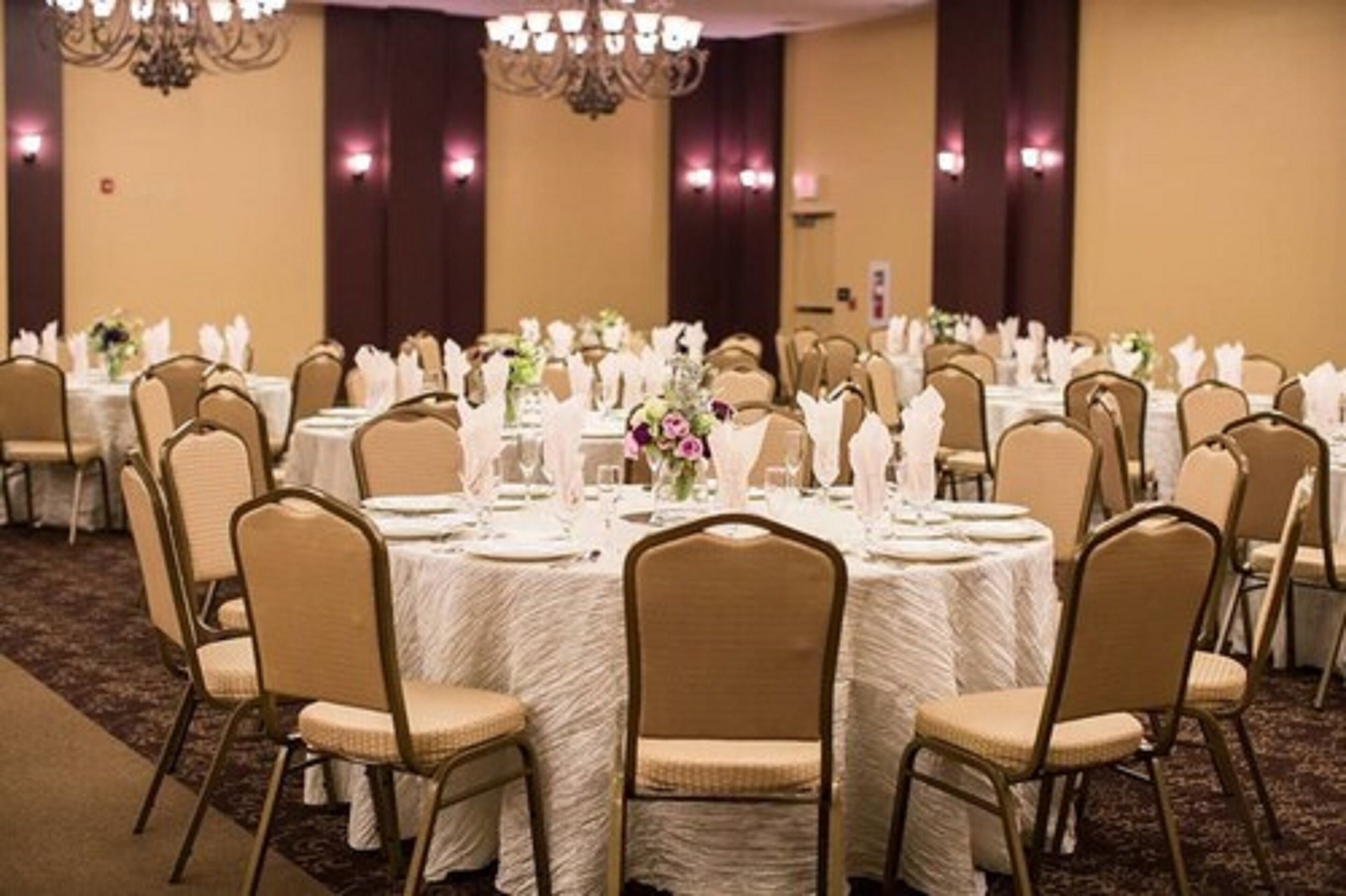 A banquet hall with round tables covered in white tablecloths, arranged in rows with chairs.