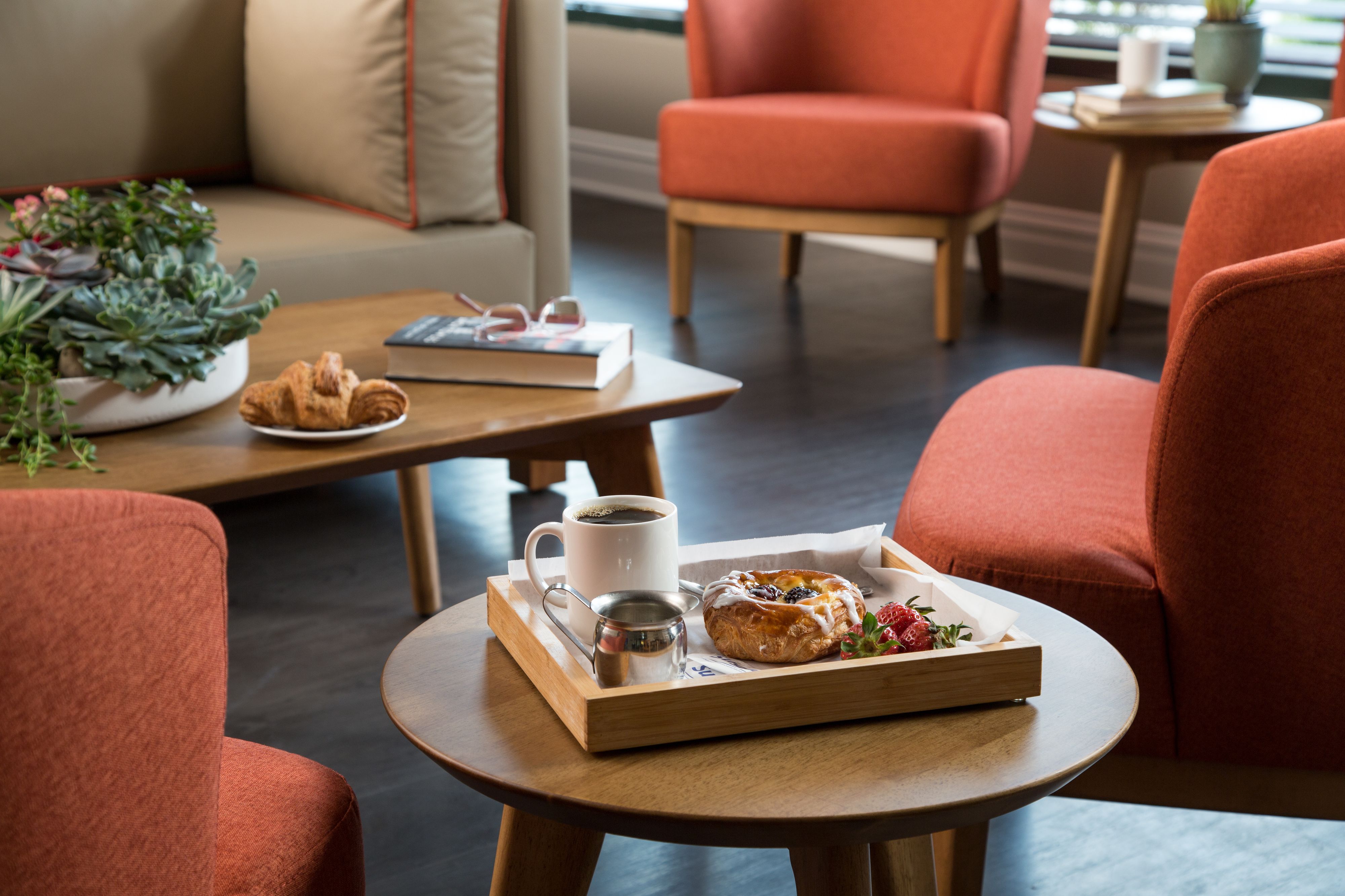 A cozy seating area with a wooden table, a tray with pastries, a cup of coffee, and a book.
