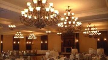 A banquet hall with multiple chandeliers, tables set for dining, and a large screen in the background.