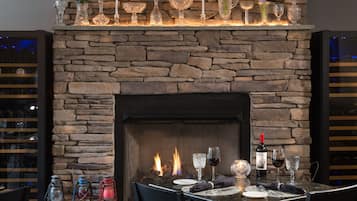 Una chimenea de piedra con una mesa de comedor dispuesta para dos personas, con una botella de vino y copas.