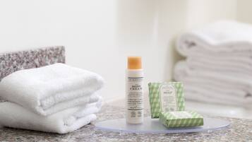 A bathroom with a granite countertop, a rolled white towel, a body cream bottle, and a soap bar.