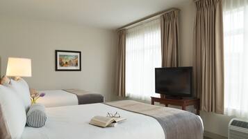 A hotel room with two beds, a television, a lamp, a picture on the wall, and a window with curtains.