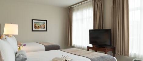 Habitación de hotel con dos camas, una televisión, una lámpara, un cuadro en la pared y una ventana con cortinas.