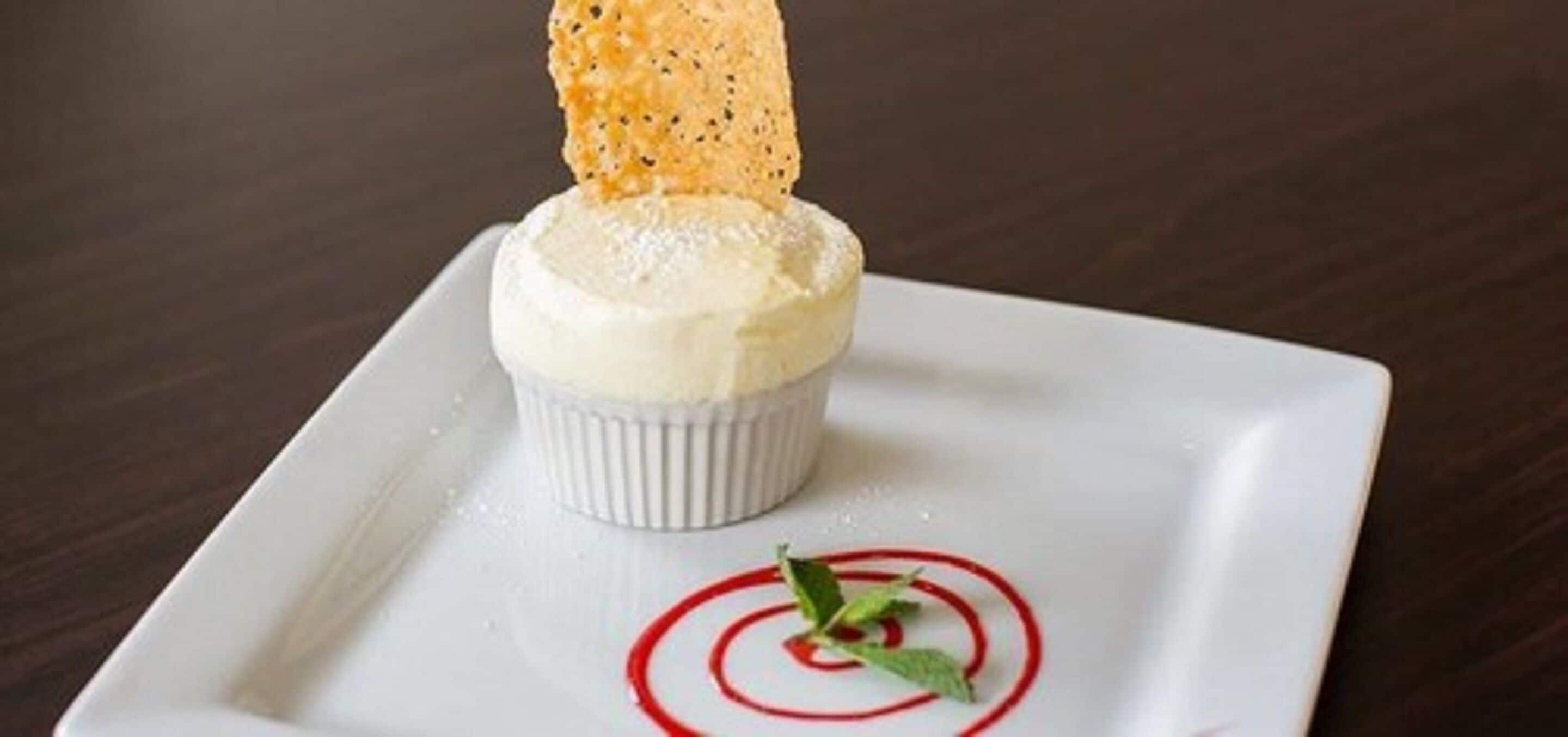 A dessert on a white plate with a red design, a biscuit, and a mint leaf garnish.