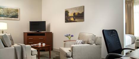 A hotel room with a sofa, armchair, TV, side table, and a painting on the wall.