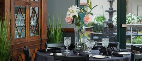 Ett dukat bord för en måltid, med en vas med blommor, klara glas och ett träskåp med glasdörrar.