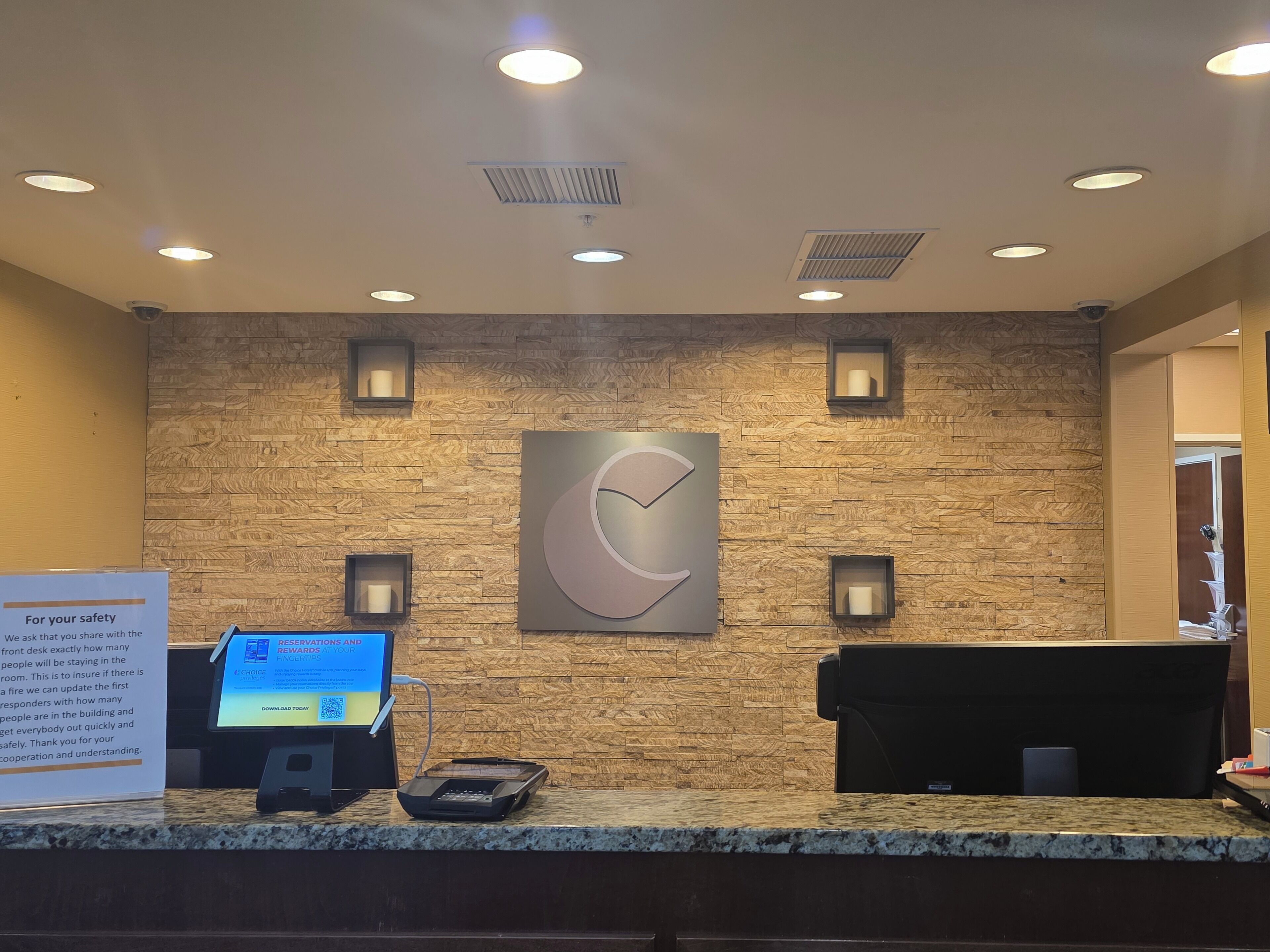 A reception desk with a digital screen, a wall-mounted logo, and a sign about safety reservations.