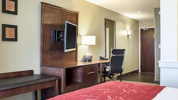 A hotel room with a bed, a desk, a chair, a TV, a lamp, and a mirror.