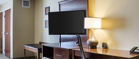 A hotel room with a desk, a television, a lamp, and a chair.