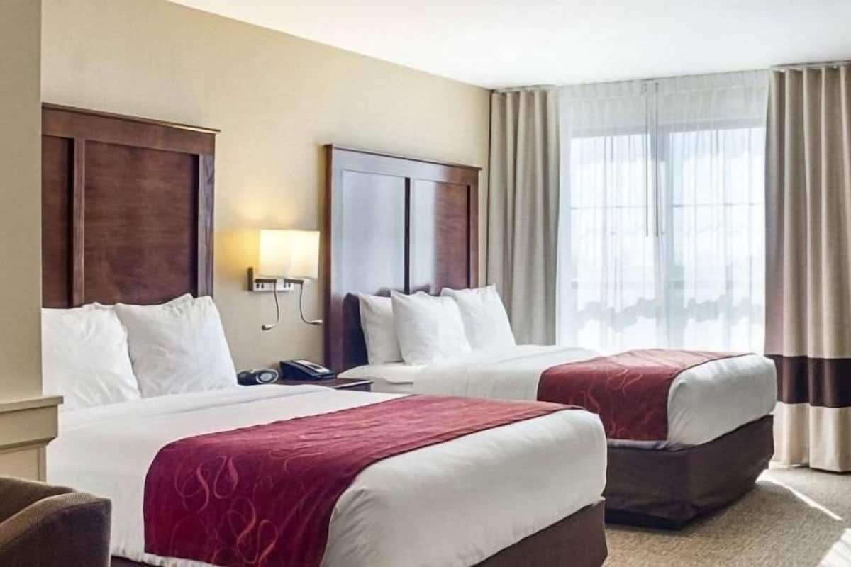 Une chambre d’hôtel avec deux lits, un bureau, une lampe et une fenêtre avec des rideaux.