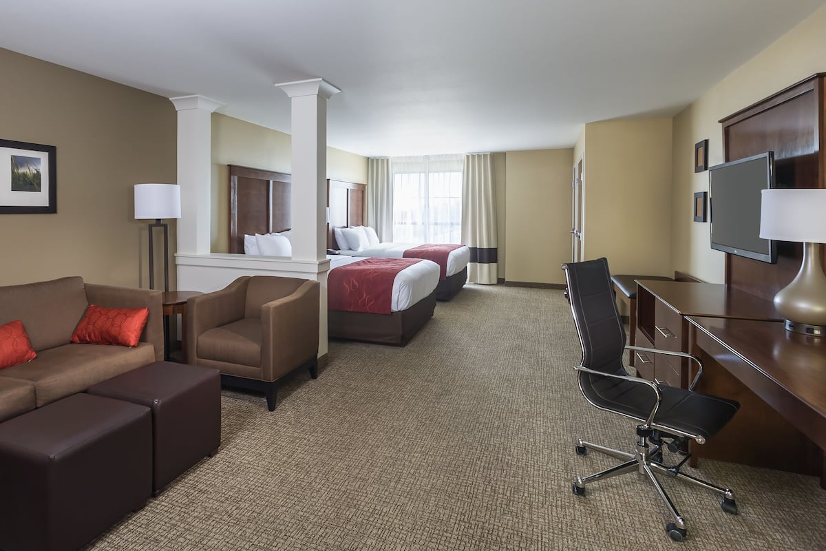 Une chambre d’hôtel avec un canapé, deux lits, un bureau, une chaise et un téléviseur.