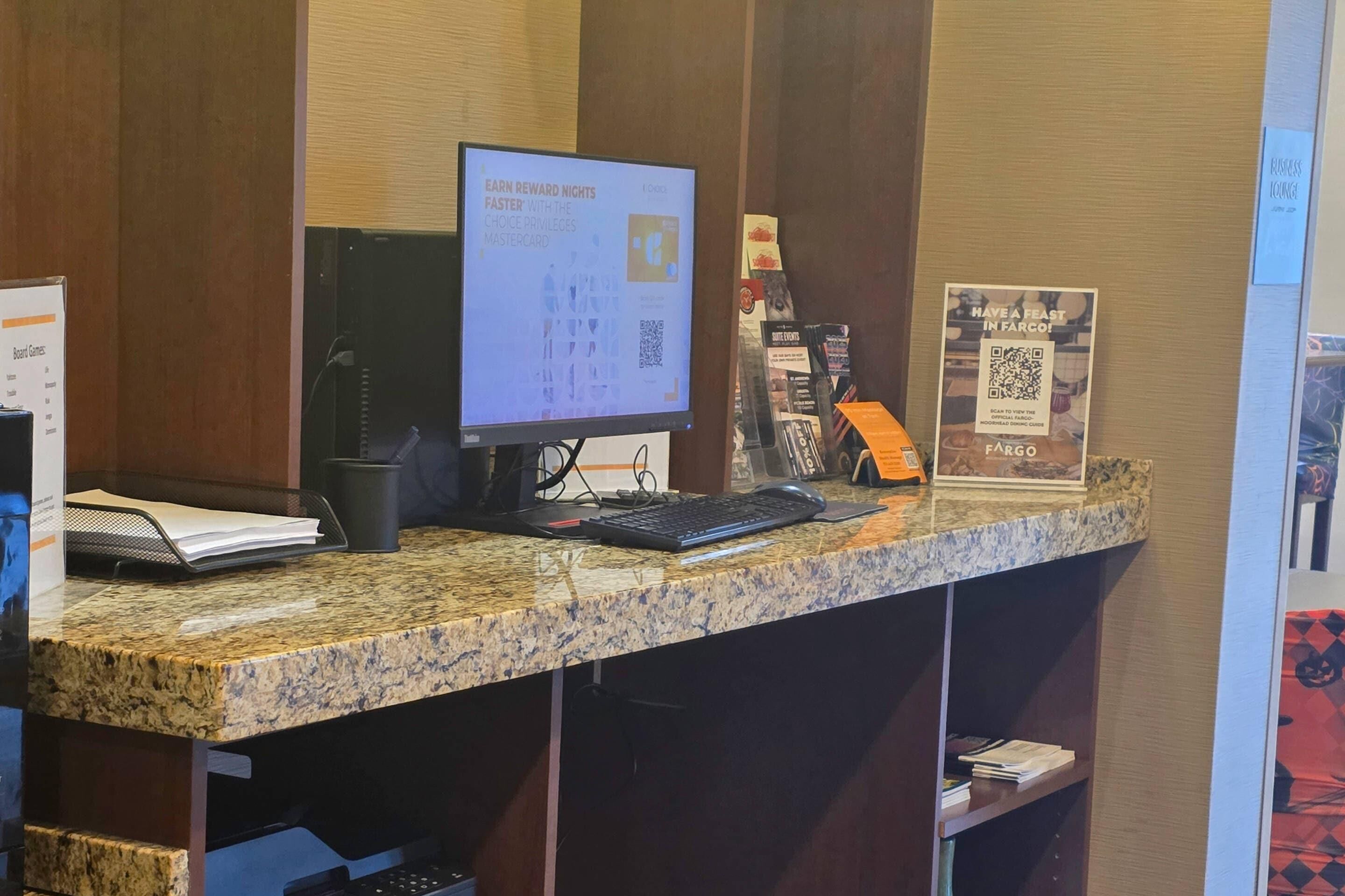 A reception desk with a computer monitor, keyboard, and mouse. There are brochures and a sign on the wall.