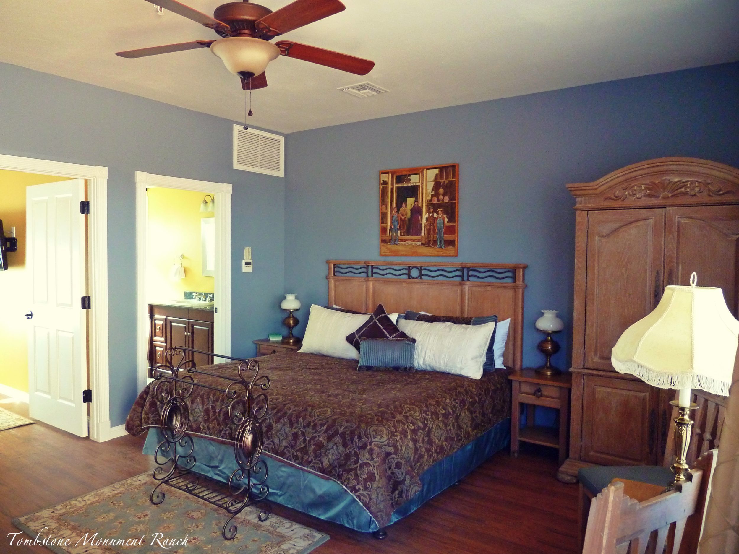 A bedroom with a bed, a ceiling fan, a wooden headboard, a nightstand, a lamp, and a dresser.