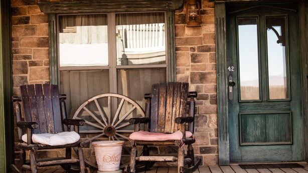 A rustic wooden porch with two rocking chairs and a large wooden wheel, a white bucket, and a green door with the number 42. - Tombstone Monument Guest Ranch (Tombstone)