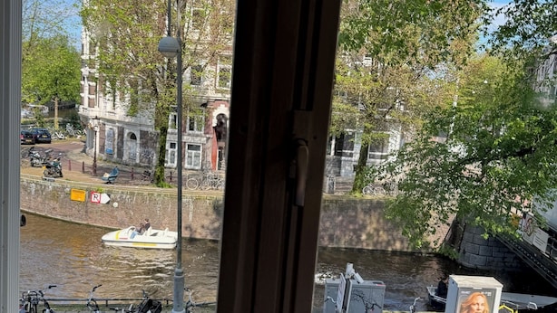 Une vue depuis une fenêtre donnant sur un canal, avec des bateaux, des vélos et des bâtiments historiques.