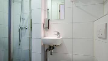 Een moderne badkamer met een douchecabine van glas, een witte wastafel en een spiegel.