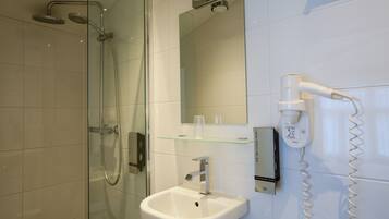 Uma casa de banho moderna com cabine de duche em vidro, lavatório branco e secador de cabelo fixado na parede.