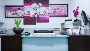 Un comptoir d’accueil avec une cloison en verre, un haut-parleur noir, une plante en pot et une œuvre d’art florale encadrée accrochée au mur.
