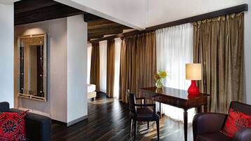 Habitación de hotel con suelo de madera oscura, un espejo grande, un escritorio con lámpara roja y un sofá con cojines rojos.
