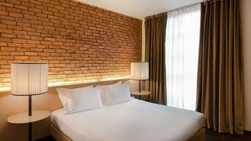 Habitación de hotel con pared de ladrillo, una cama grande con ropa de cama blanca, dos lámparas de noche y una ventana con cortinas.