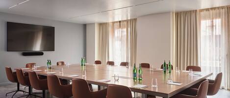 Ein Konferenzraum mit einem langen Tisch, braunen Stühlen und einem Flachbildfernseher an der Wand.