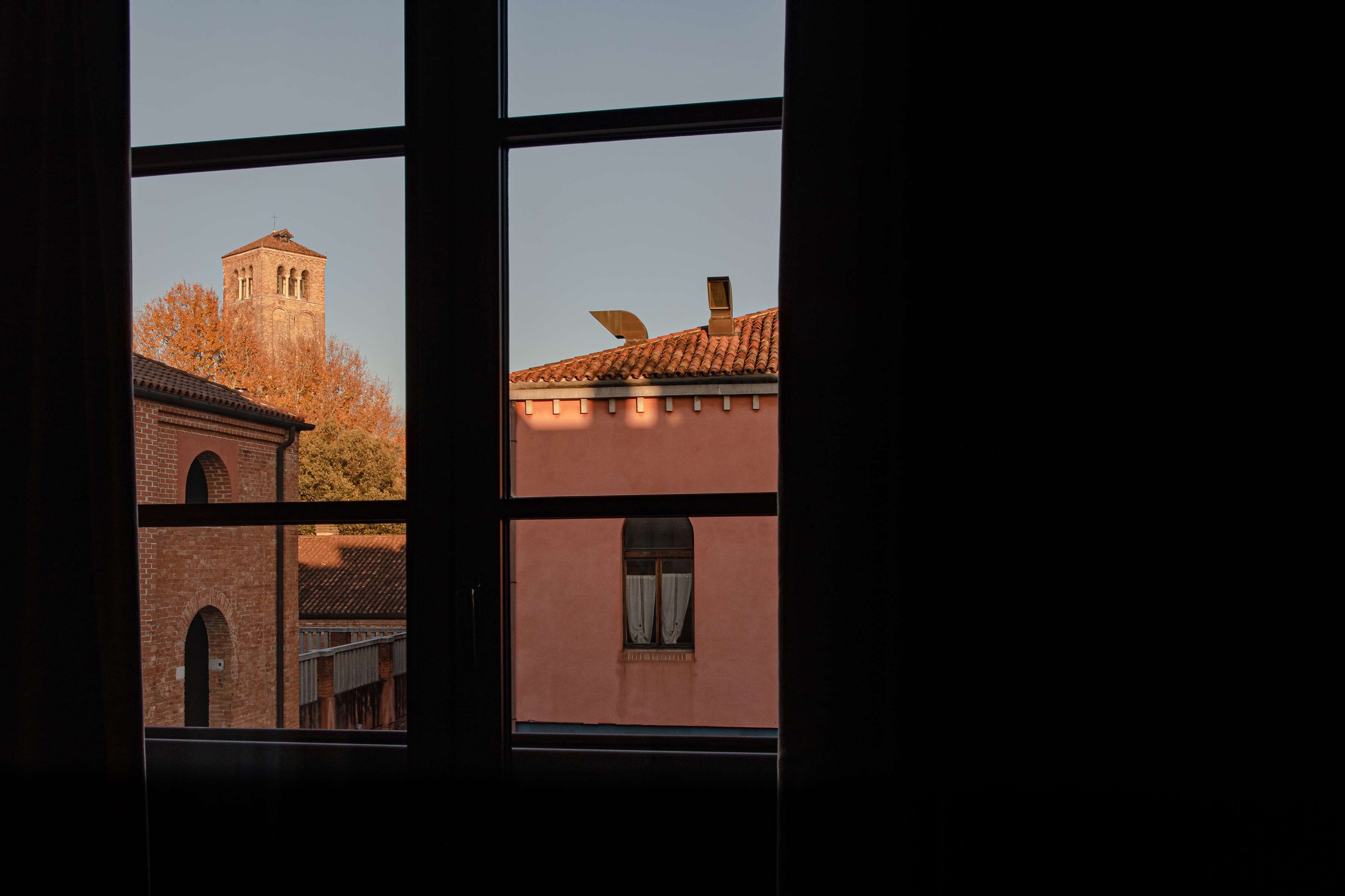 A view through a window of a building with a brick facade, a tiled roof, and a bell tower.