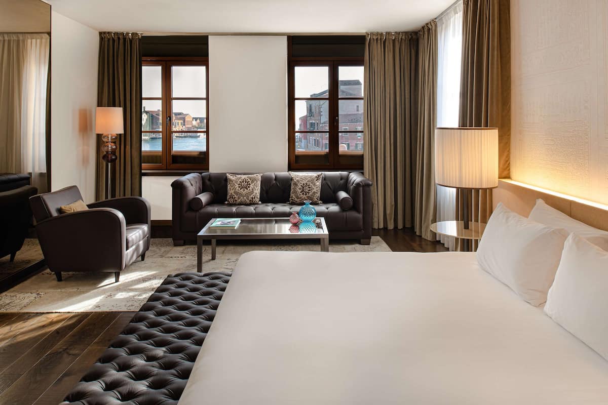 Une chambre d’hôtel avec un grand lit, un canapé, une table basse et une vue sur la ville grâce à de grandes fenêtres.