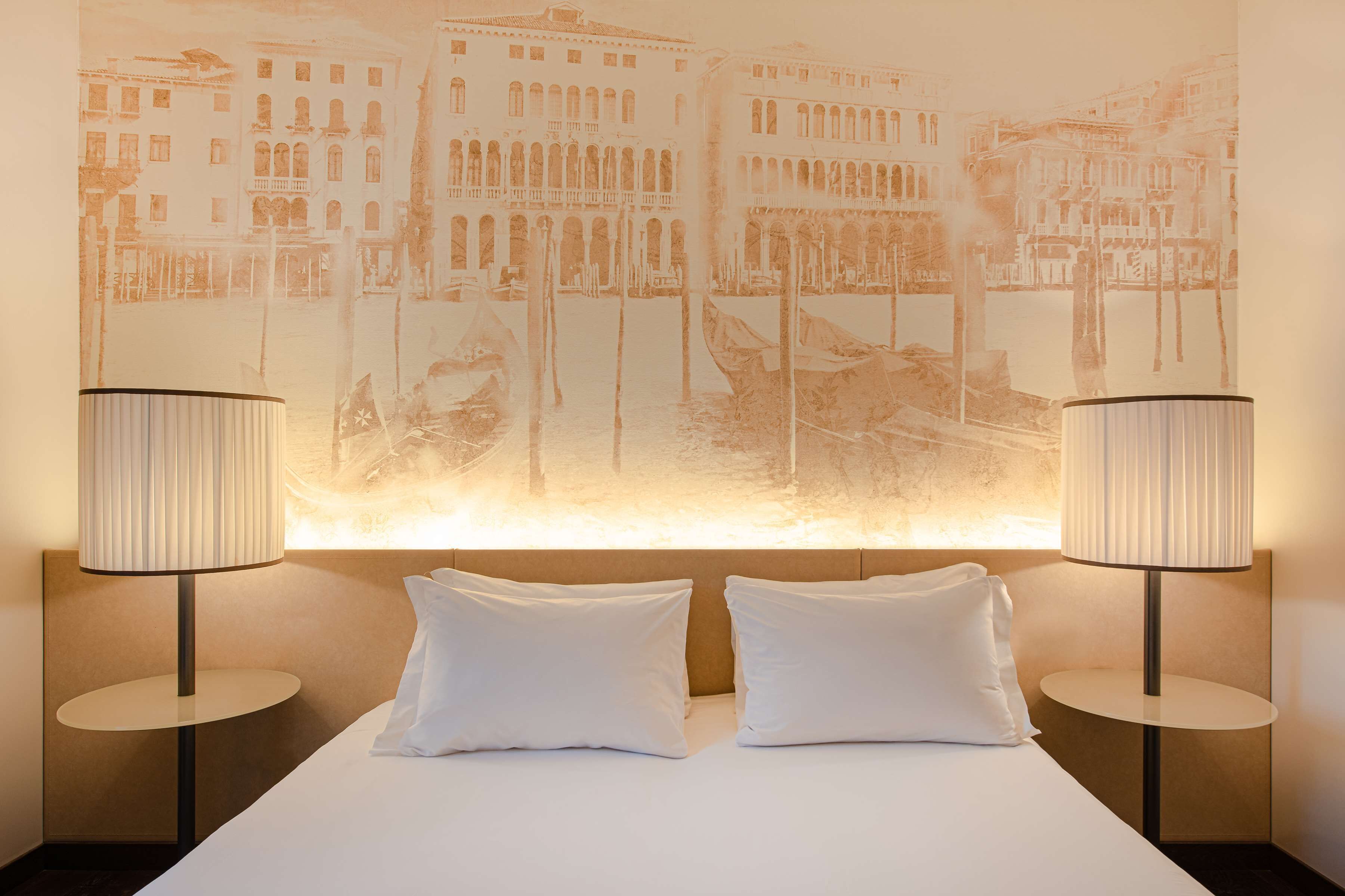 Ett hotellrum med en säng, två sänglampor och en stor väggmålning.