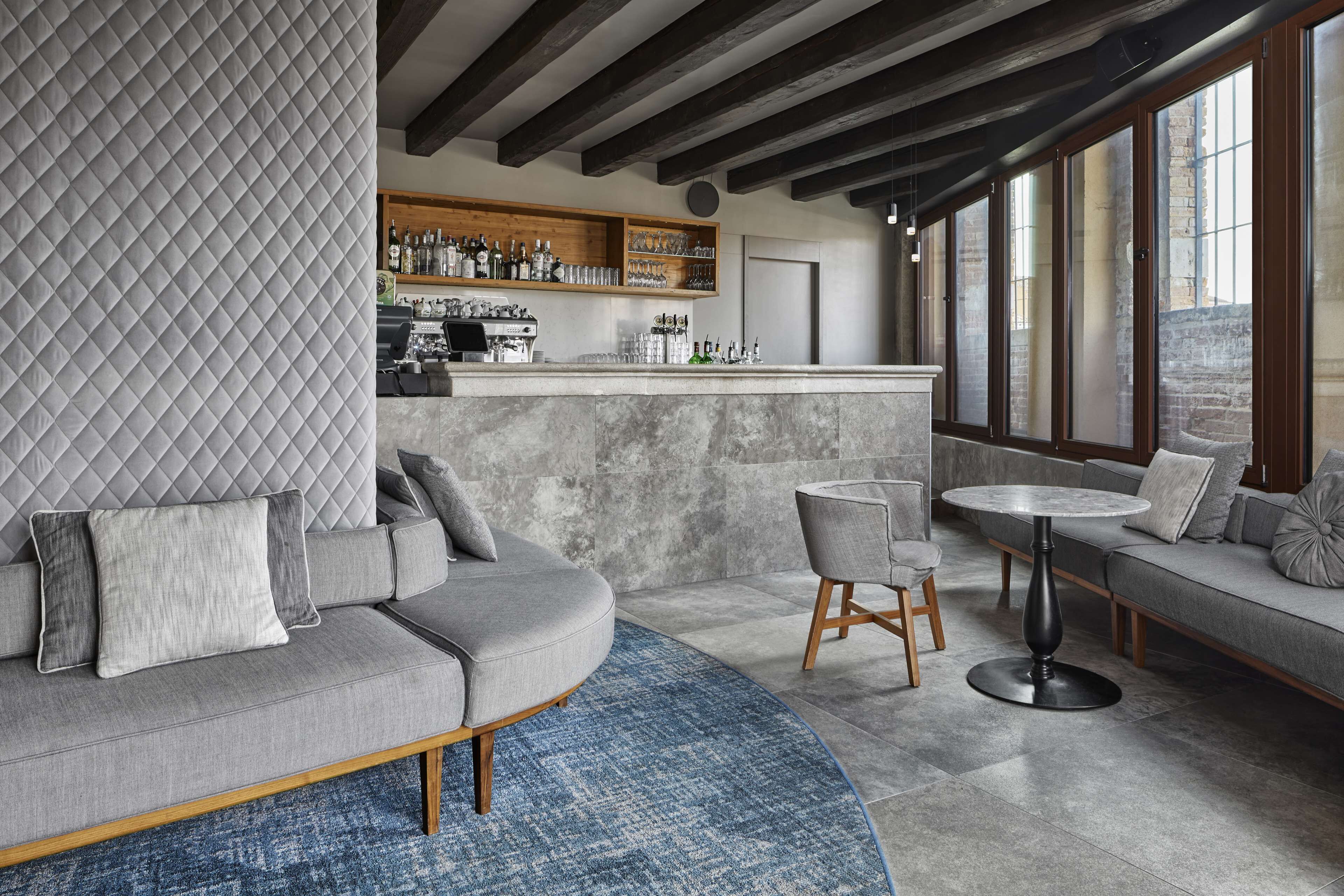A modern bar area with a curved sofa, a round table, and a bar counter with shelves of bottles and glasses.