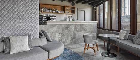 Un espace bar moderne avec un canapé incurvé, une table ronde et un comptoir de bar doté d’étagères remplies de bouteilles et de verres.