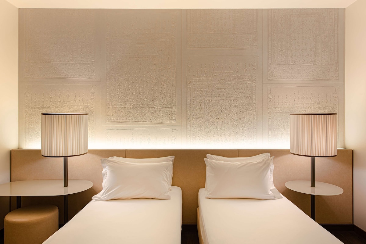 Une chambre d’hôtel avec deux lits, une table ronde et une lampe.