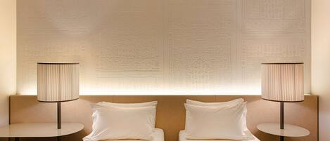 A hotel room with two beds, a round table, and a lamp.