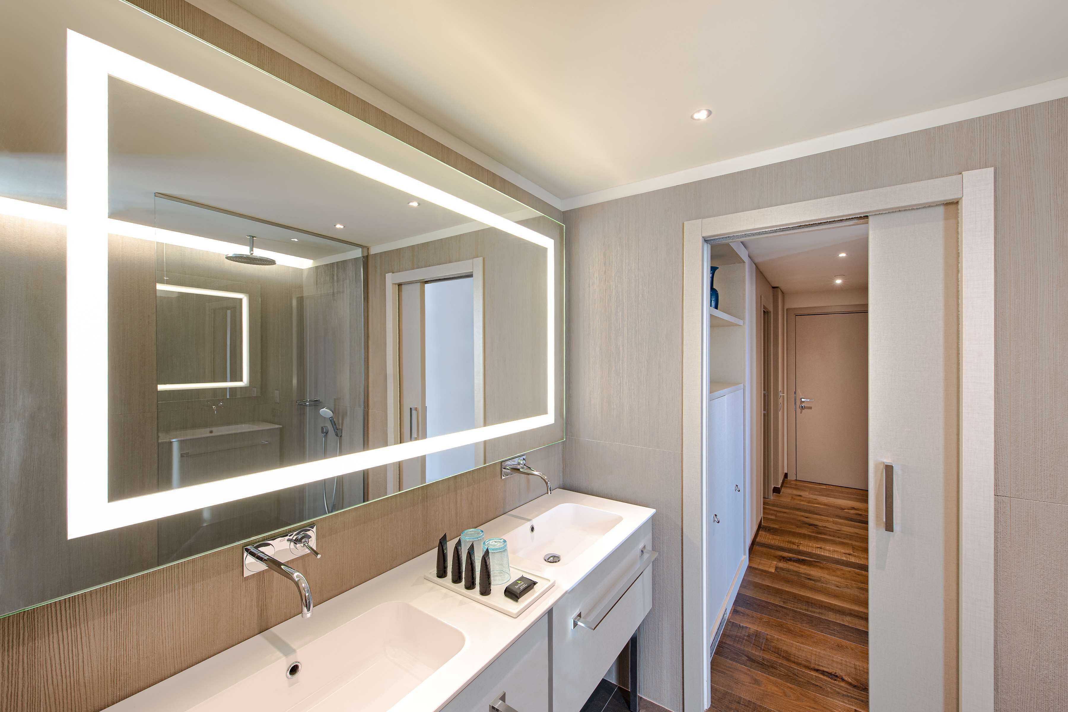 Un bagno moderno con due lavabi, uno specchio grande e un pavimento in legno.