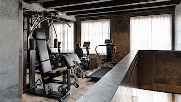 A modern gym with exercise equipment, large windows, and a stone-tiled floor.