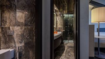 A modern bathroom with a marble wall, a glass shower enclosure, and a round table with a lamp.