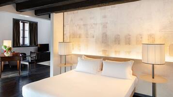 A hotel room with a large bed, two bedside lamps, a desk with a chair, and a wall with a historical mural.