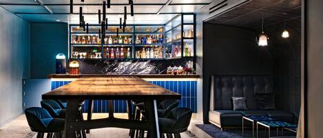 A bar area with a wooden table and chairs, a seating area with a sofa and a small table, and a wall with shelves of bottles.