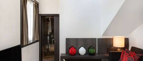 Una sala moderna con un banco de madera oscura, un sofá y un televisor. Hay tres jarrones decorativos sobre el banco y una lámpara en el sofá.