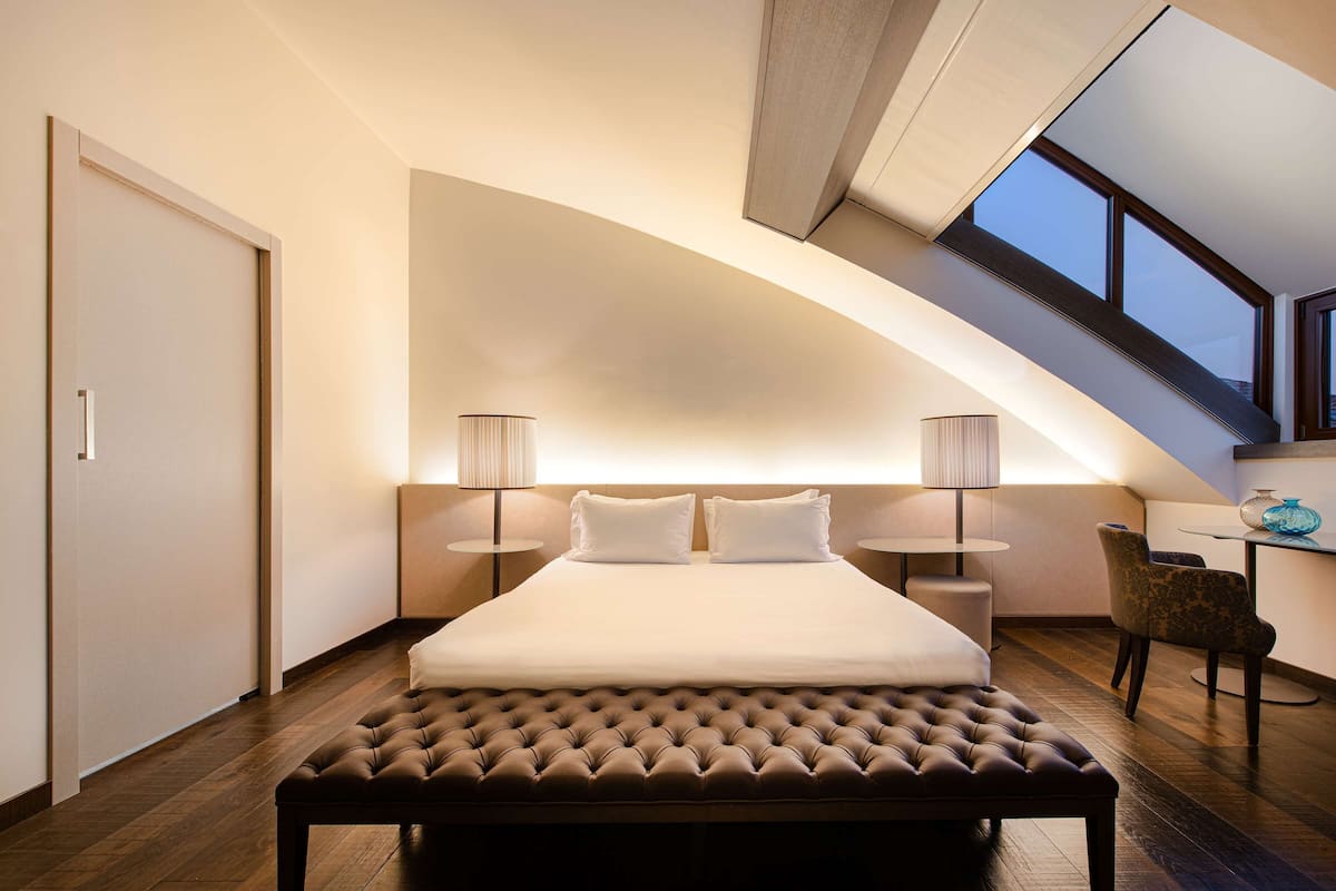 Une chambre à coucher moderne avec un grand lit, deux lampes de chevet, un banc et un bureau avec une chaise.