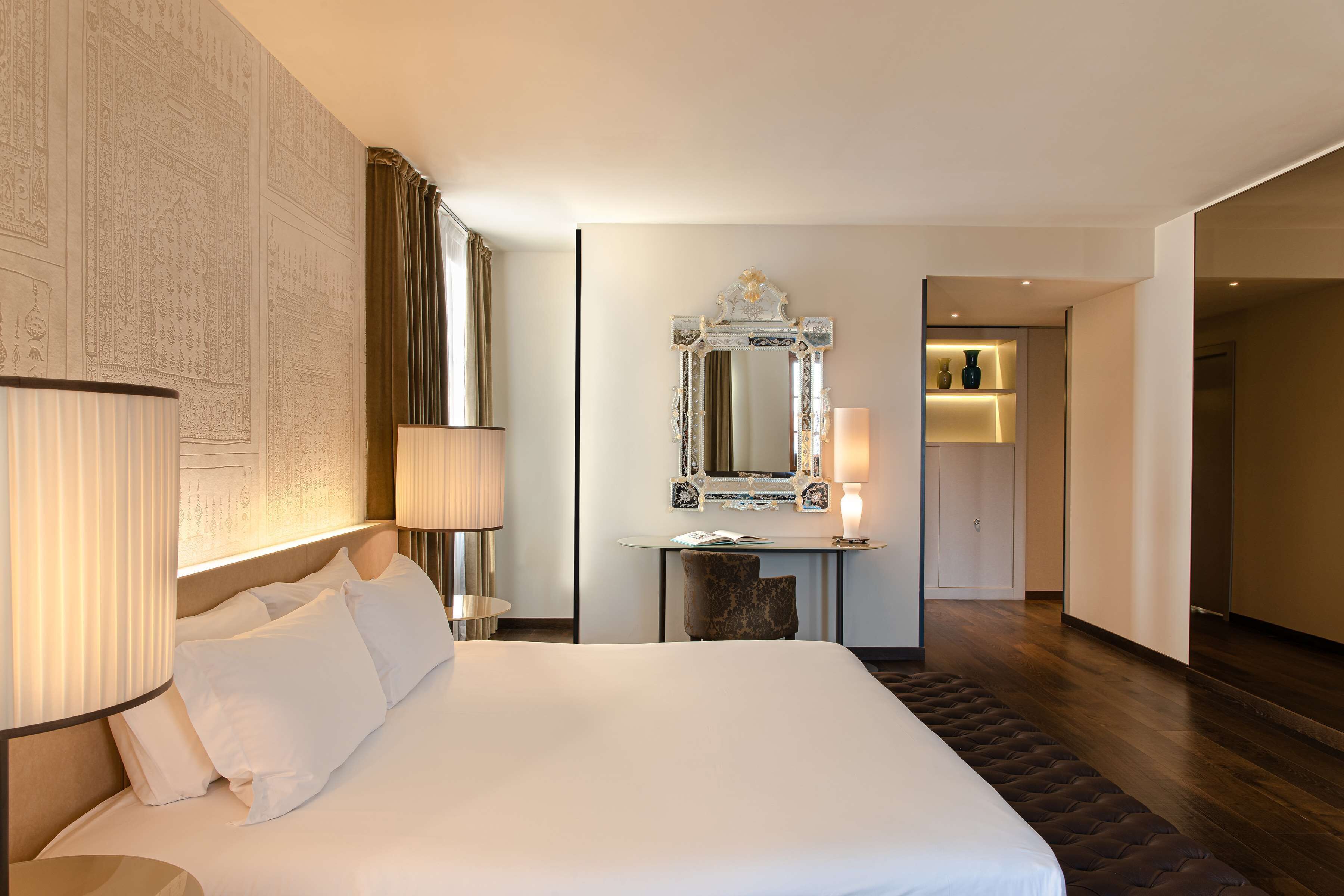 Quarto de hotel com uma cama grande, uma escrivaninha com espelho e uma luminária.